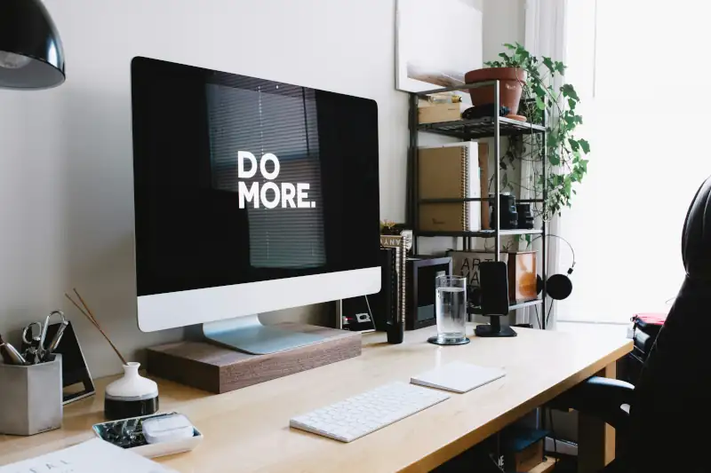 A computer sitting on a wooden desk. The screen reads 'Do More.'